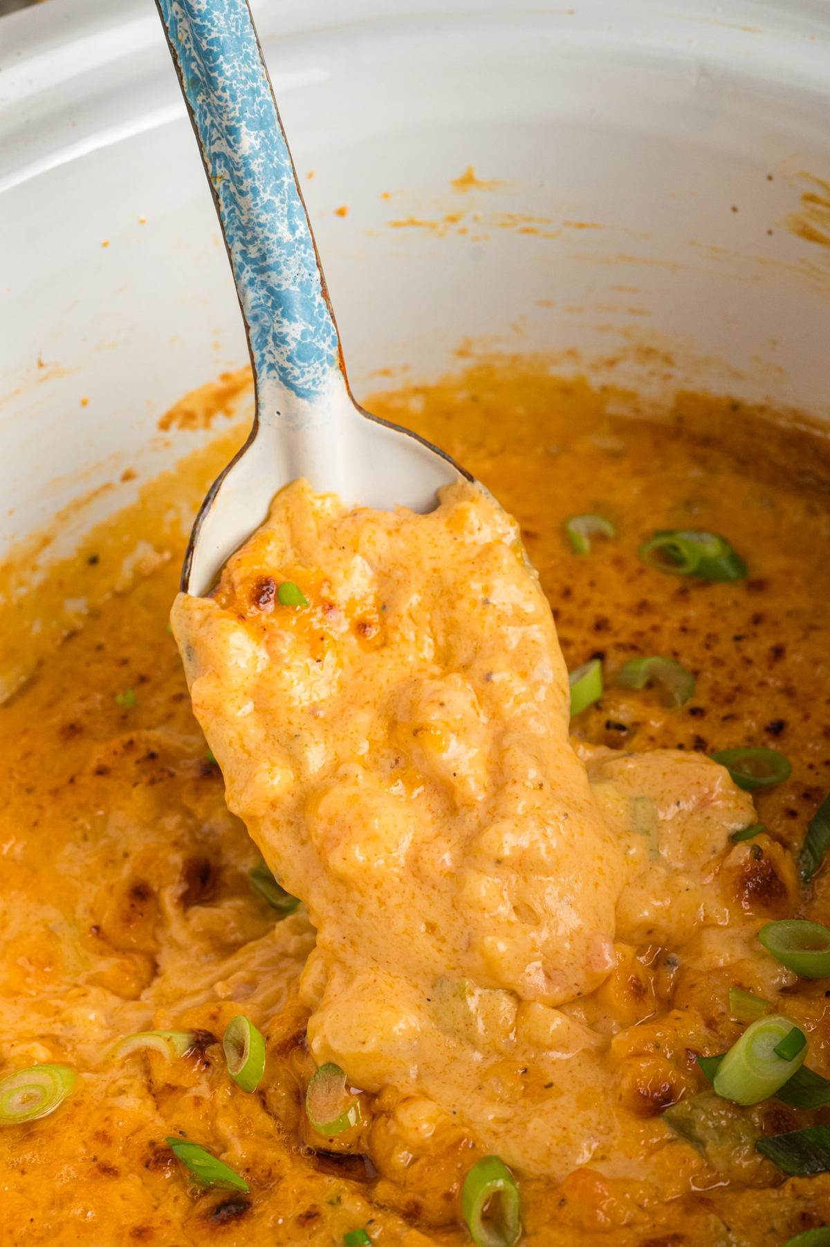 scooping hot shrimp dip out of slow cooker with a spoon.
