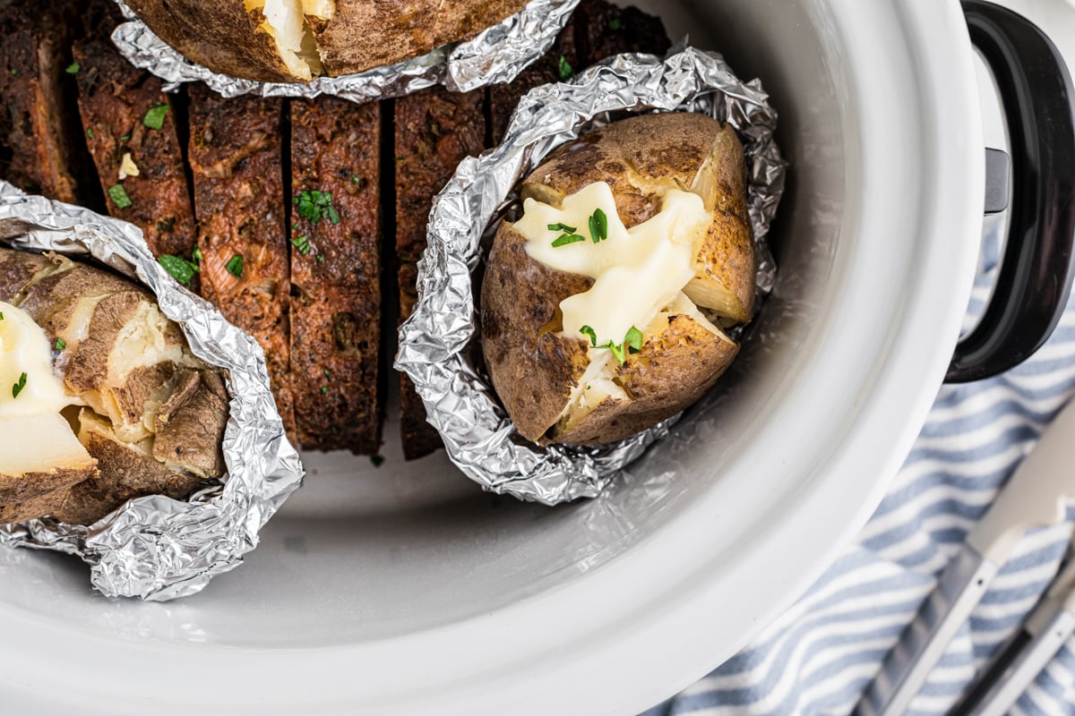 overhead of slow cooker meatloaf and baked potatoes.