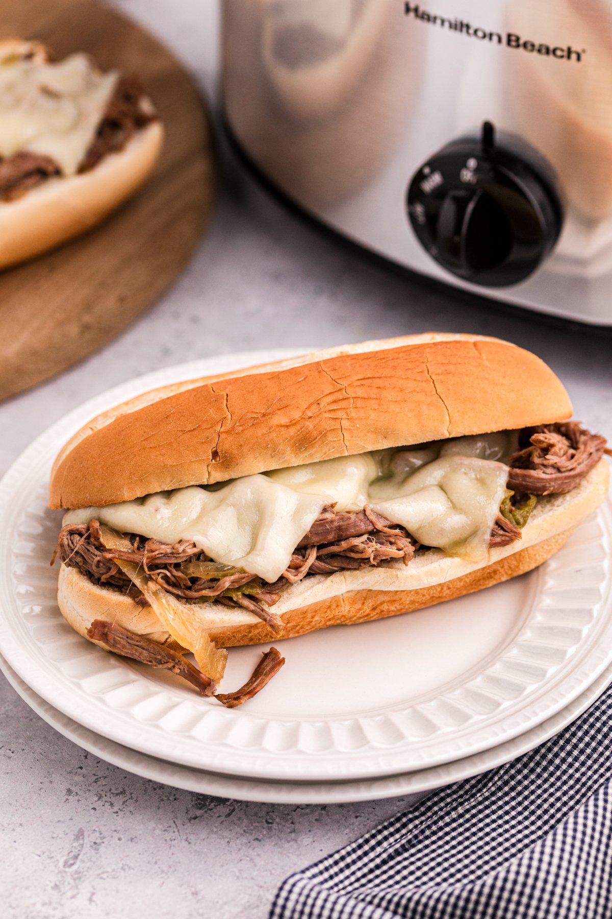 slow cooker philly cheese steak sandwich on stack of plates.
