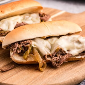 two slow cooker philly cheese steak sandwiches on a wooden board.