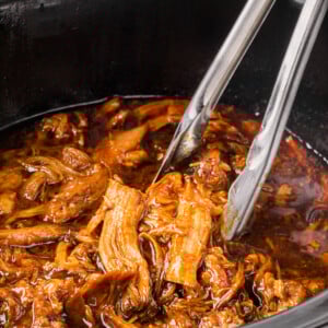 root beer pulled pork in a slow cooker with tongs.