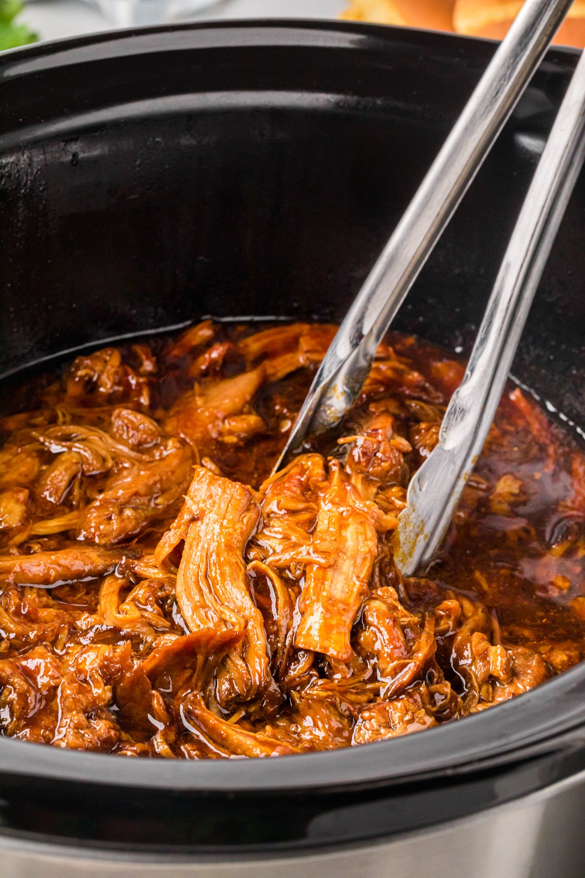 root beer pulled pork in a slow cooker with tongs.