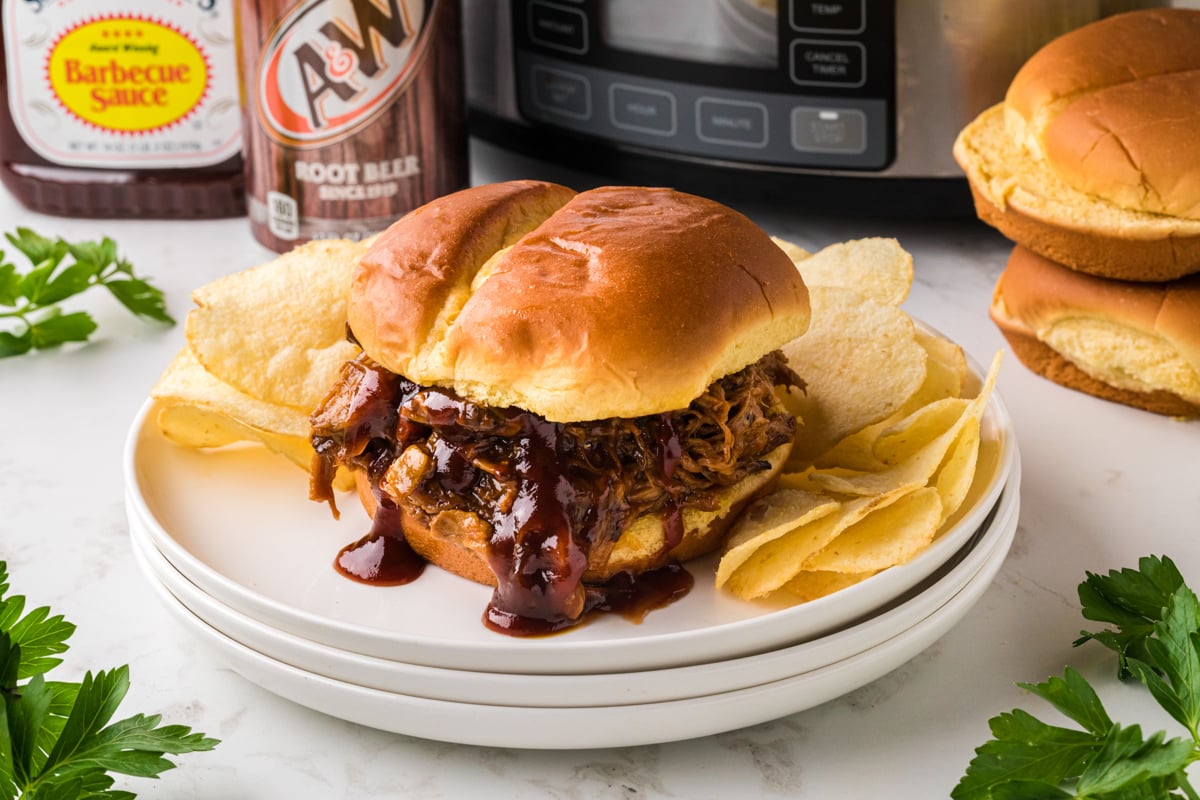 slow cooker root beer pulled pork sandwich on a stack of plates.