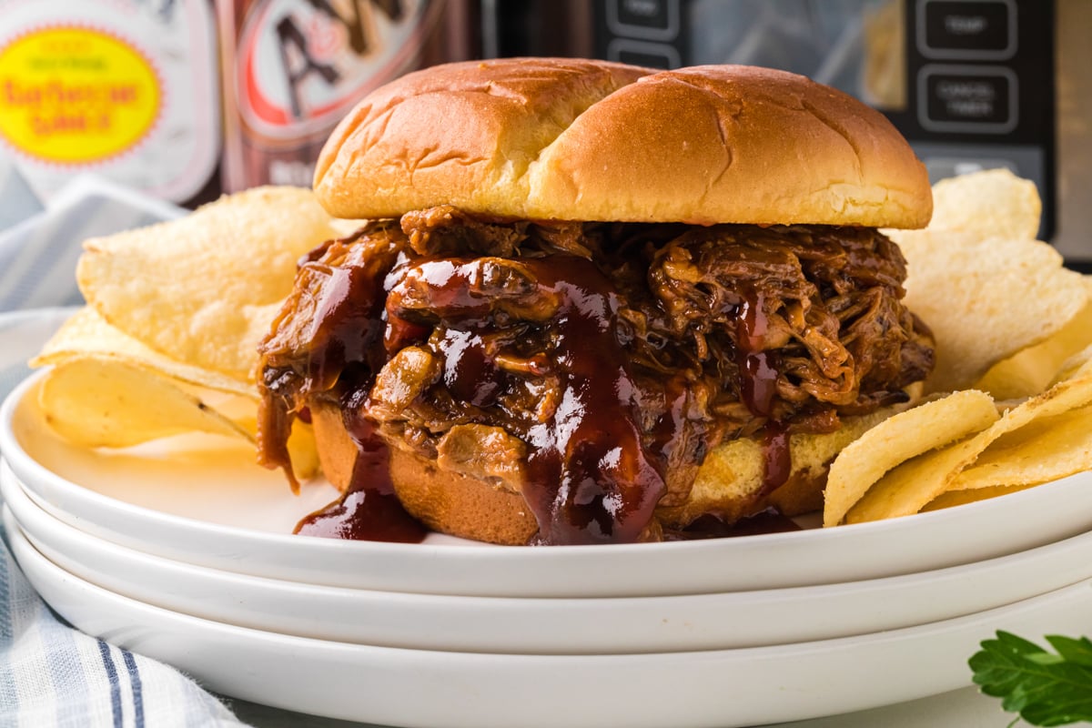 close-up of slow cooker root beer pulled pork sandwich on stack of white plates.