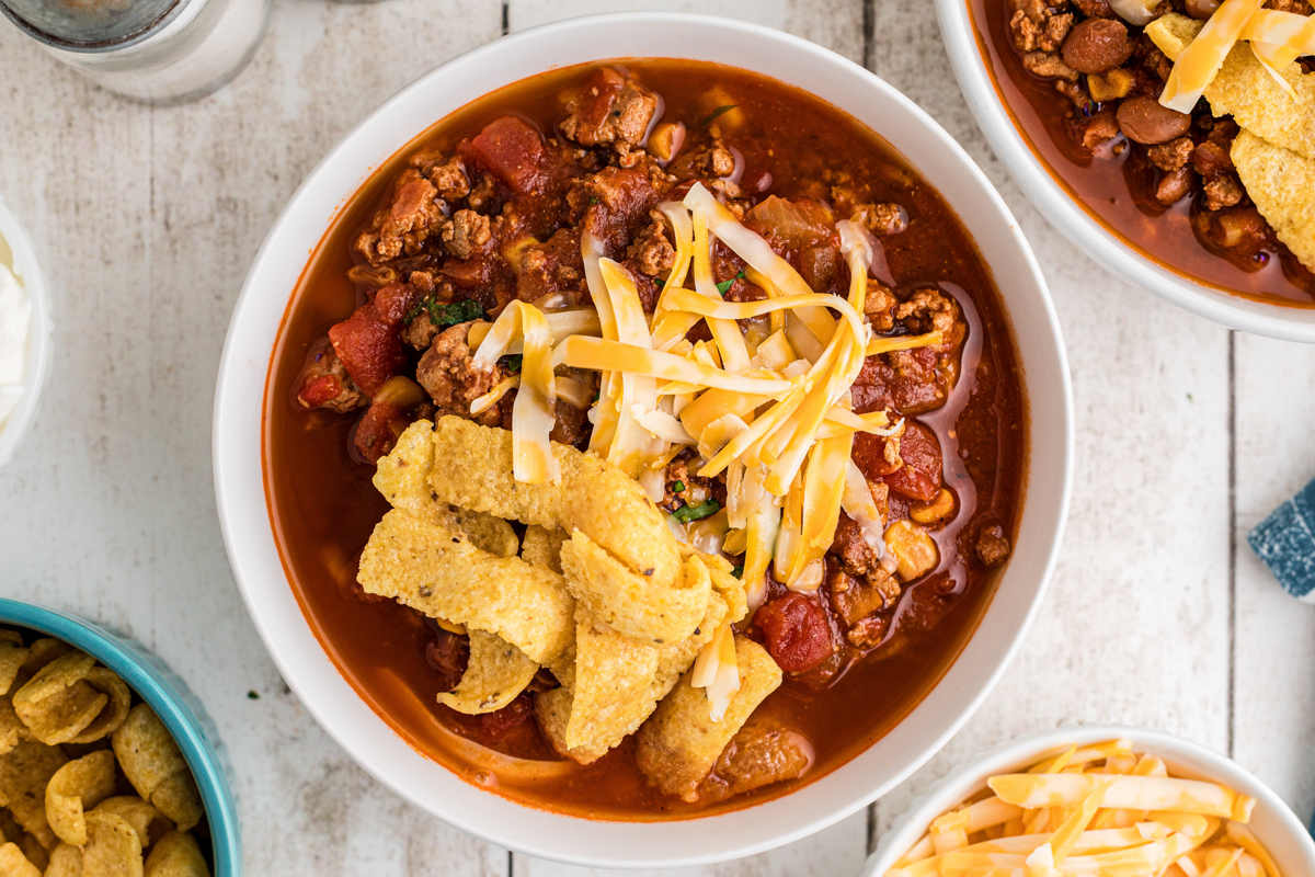 overhead of slow cooker turkey chili in a bowl with cheese and corn chips on top.