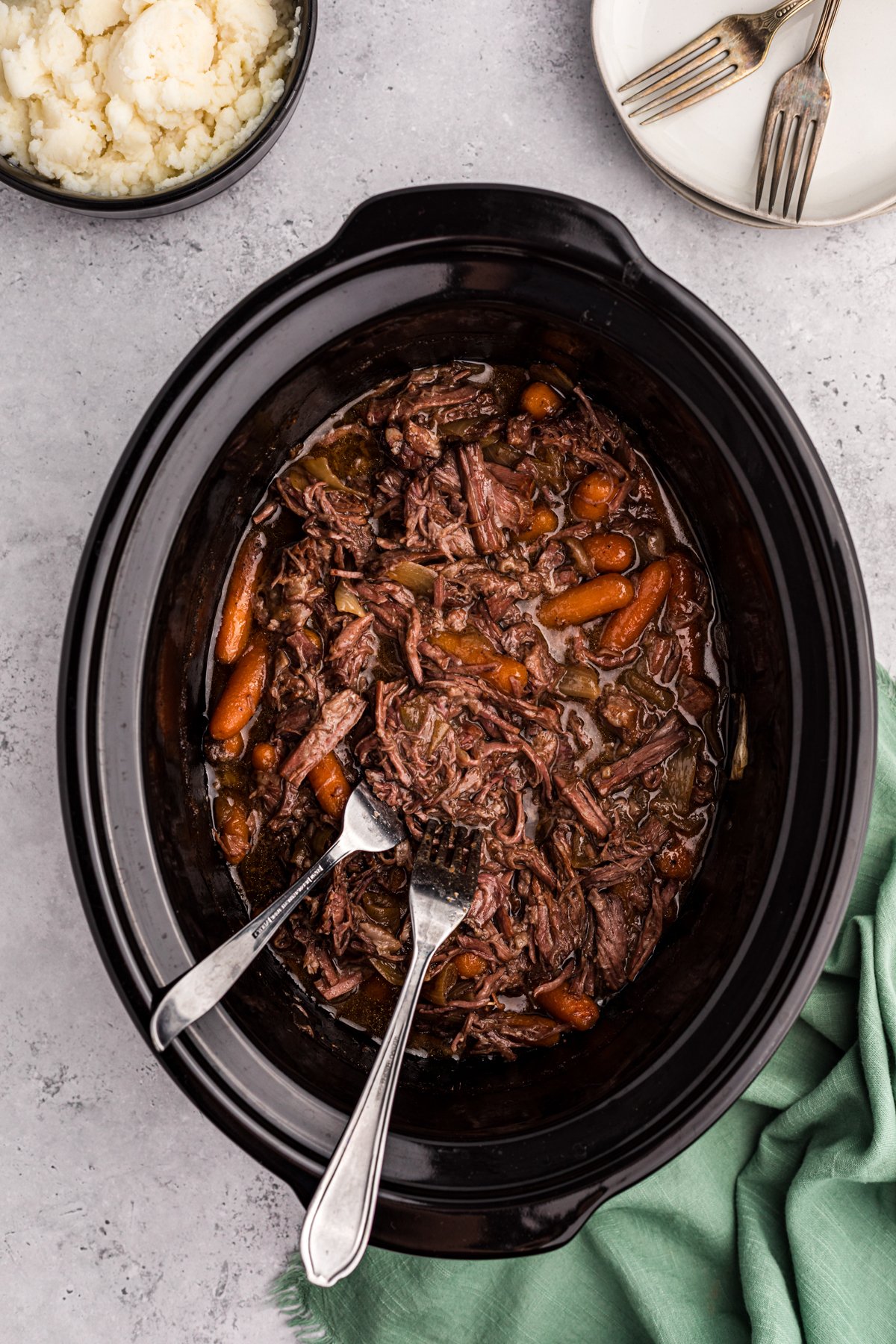 Shredded three packet pot roast with carrots in a slow cooker.