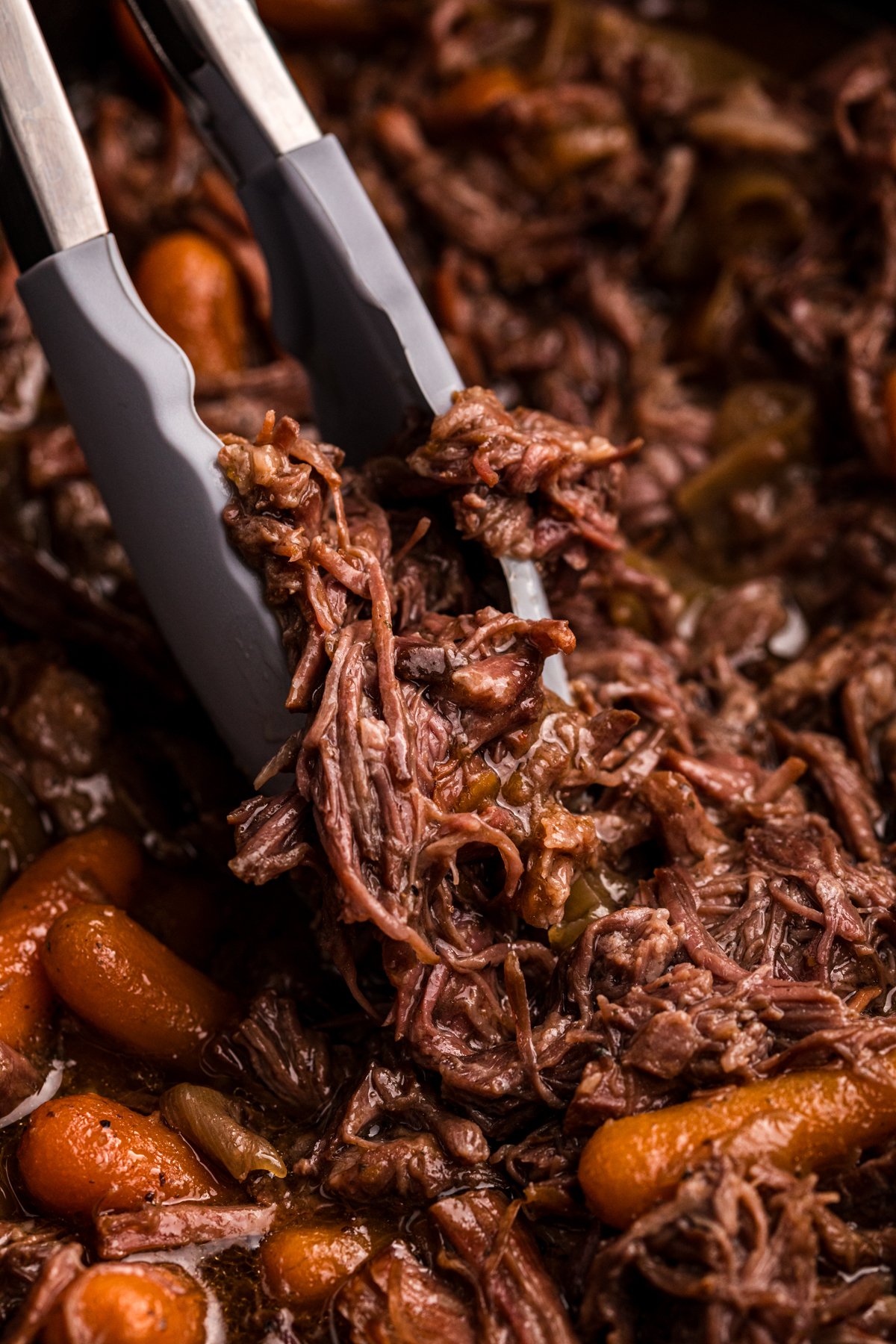tongs grabbing some slow cooker 3 packet roast.