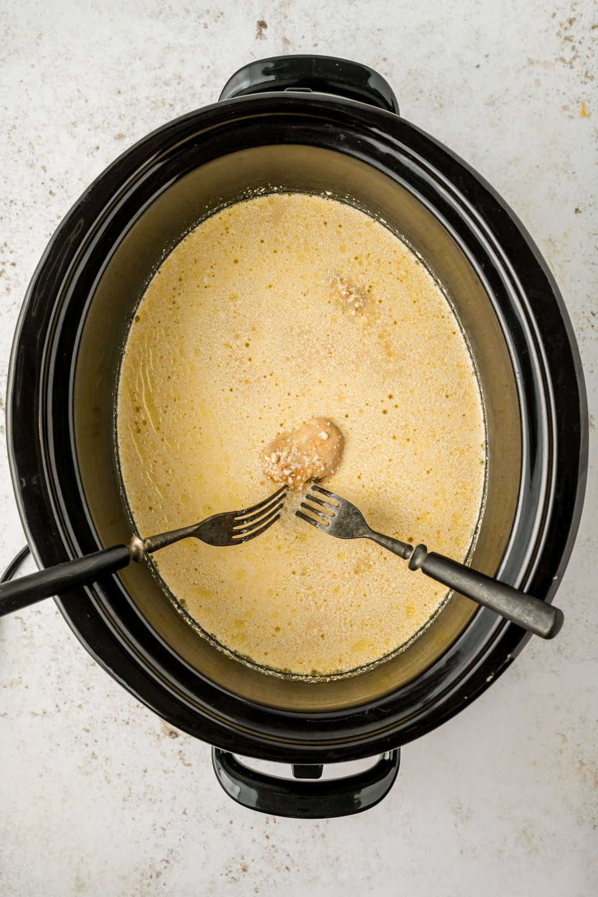 chicken being shredded in a slow cooker.