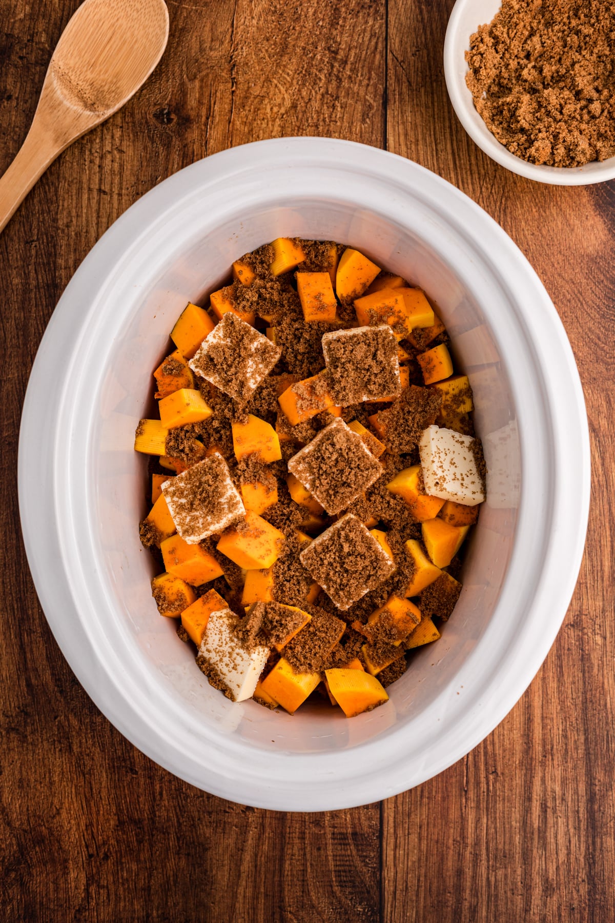 Cubed butternut squash in a slow cooker with seasonings and butter.