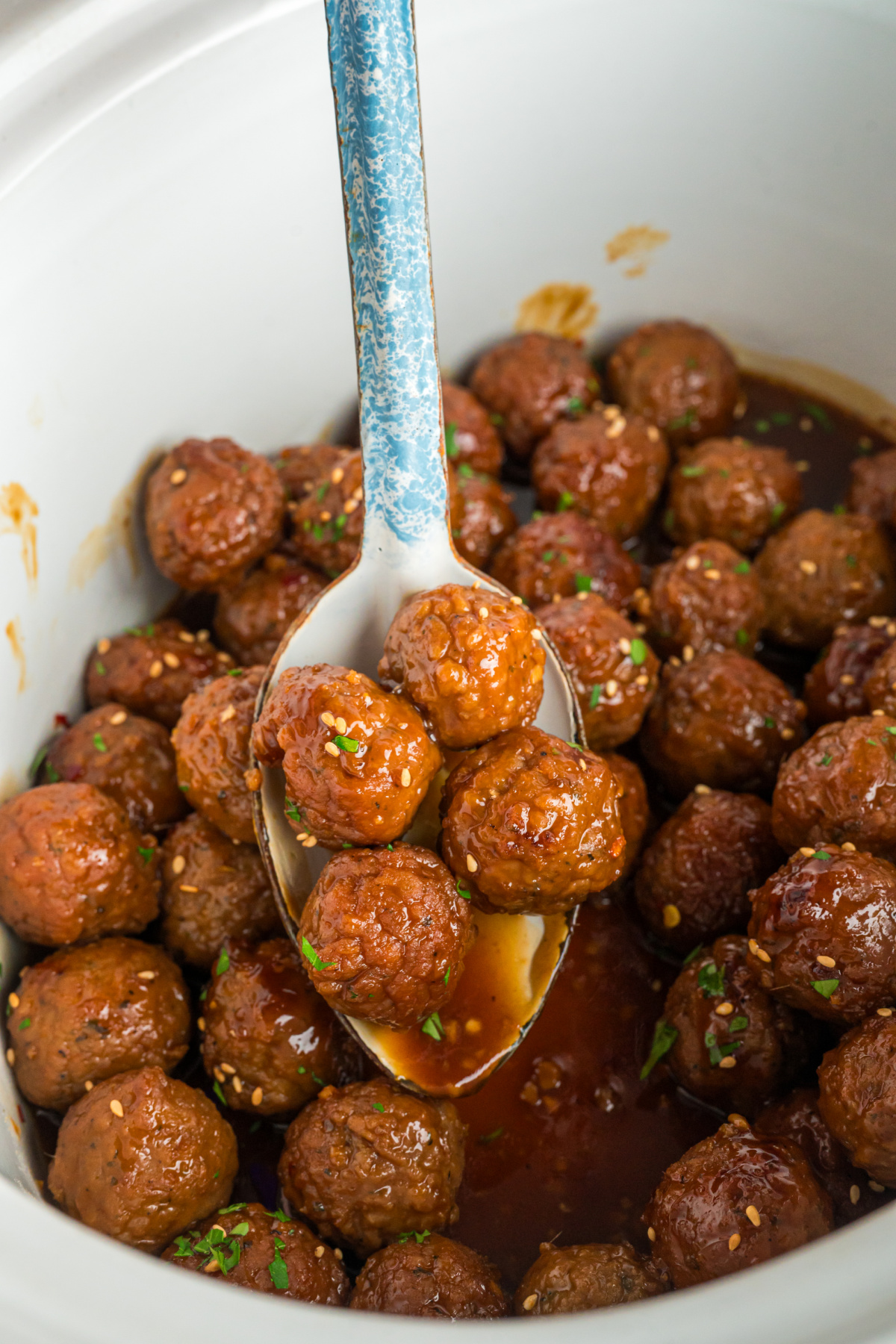 Cooked honey garlic meatballs on a spoon and in a slow cooker.