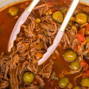 pulling some ropa vieja out of a slow cooker with tongs.