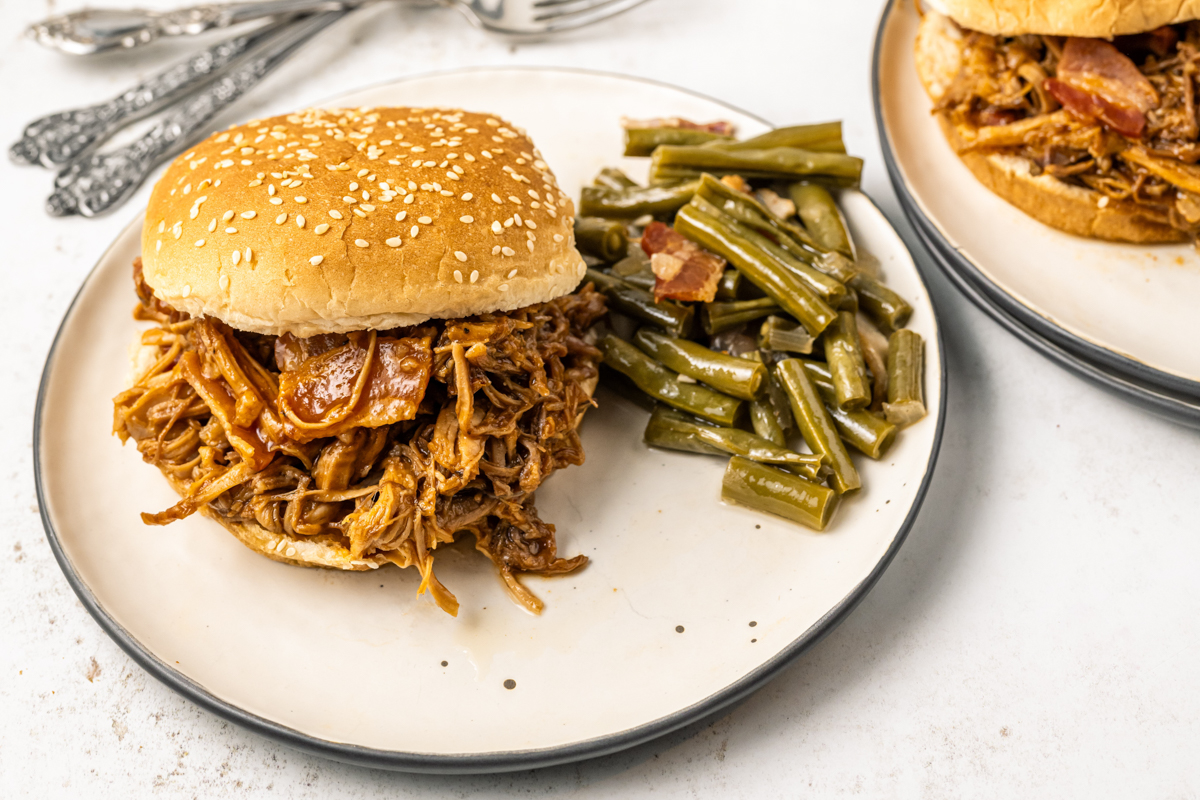 slow cooker bourbon bacon pulled pork on a bun with green beans on the side.