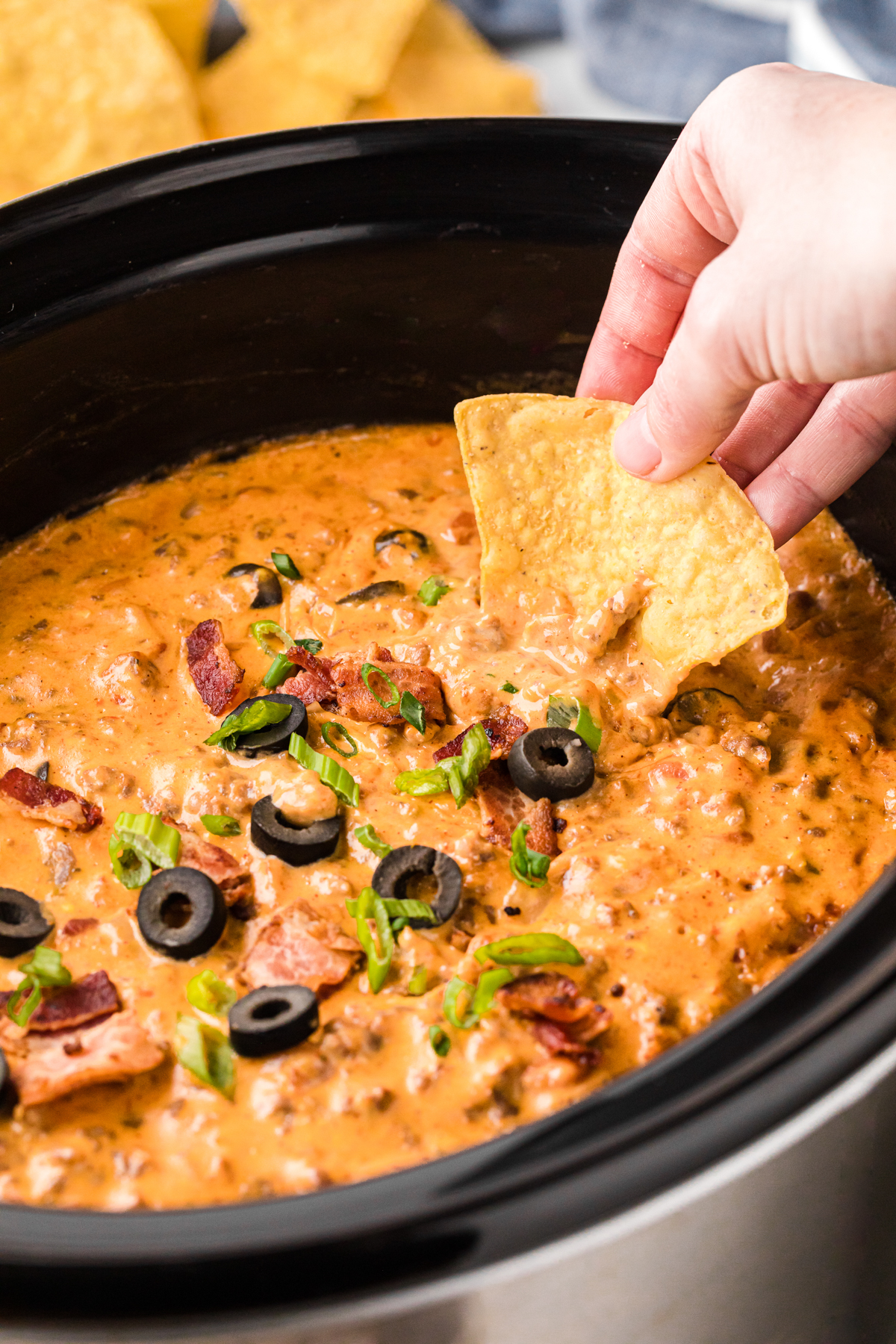 scooping loaded nacho dip with a tortilla chip from a slow cooker.