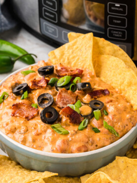 slow cooker loaded nacho dip in a white bowl with chips in and around it.