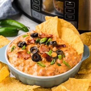slow cooker loaded nacho dip in a white bowl with chips in and around it.