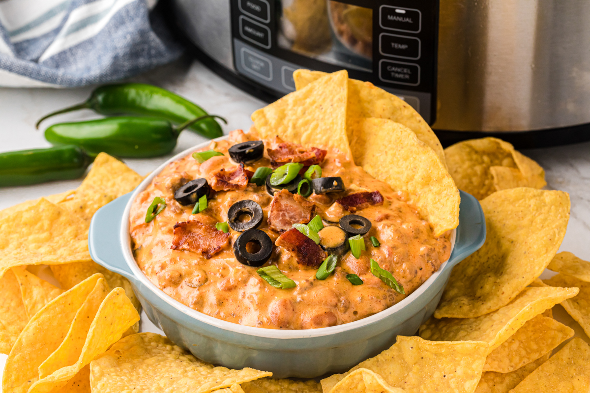  slow cooker loaded nacho dip in a white bowl with chips in and around it.
