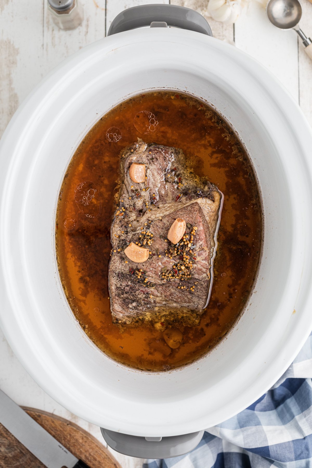 Cooked pastrami in a crockpot, with juices around it.