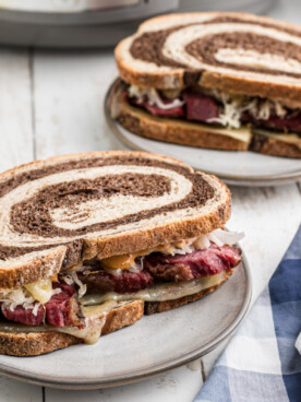 two slow cooker pastrami sandwiches on plates.