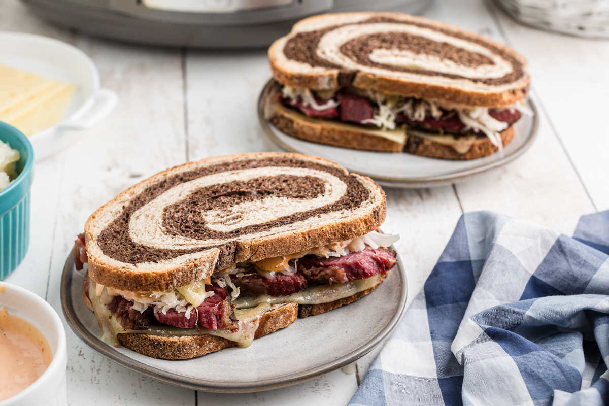 two slow cooker pastrami sandwiches on plates.
