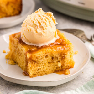 piece of slow cooker caramel cake on a plate with ice cream on top.
