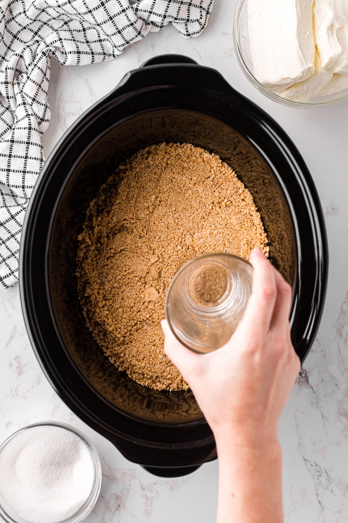 graham cracker mix being tamped down in slow cooker for cheesecake.