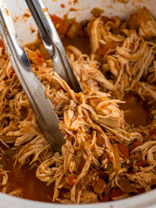 tongs grabbing meat for chicken tacos from a slow cooker.