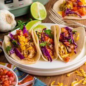 three slow cooker chicken tacos on a stack of plates.