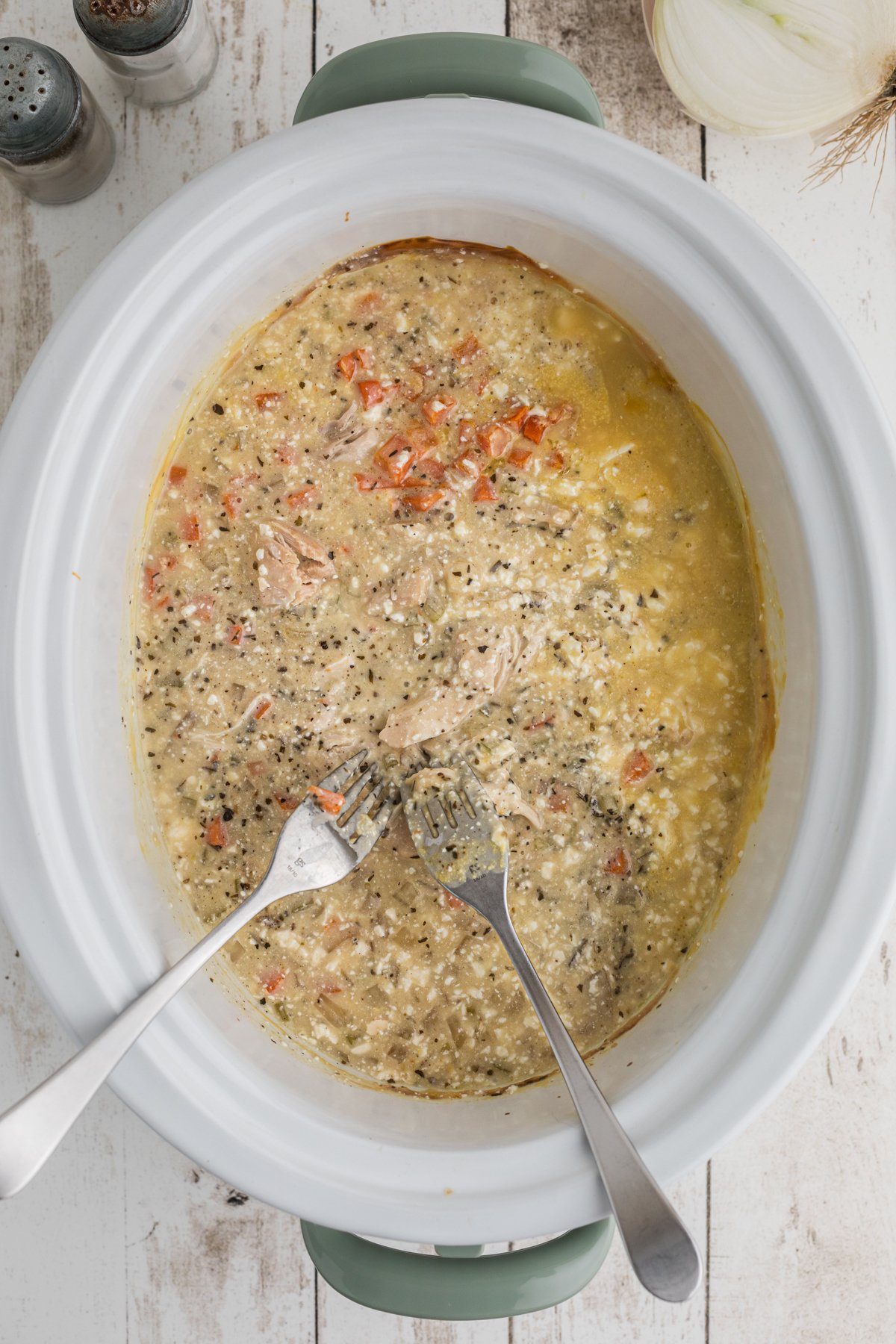 chicken being shredded in the slow cooker with two forks.
