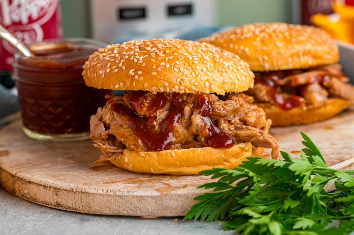 two slow cooker dr. pepper pulled pork sandwiches on a wooden board.