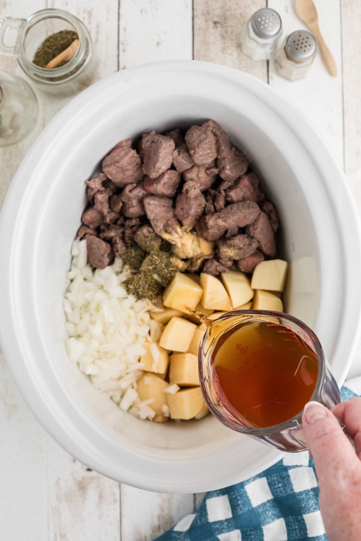 beef broth being pour into slow cooker with potatoes, beef and onions.