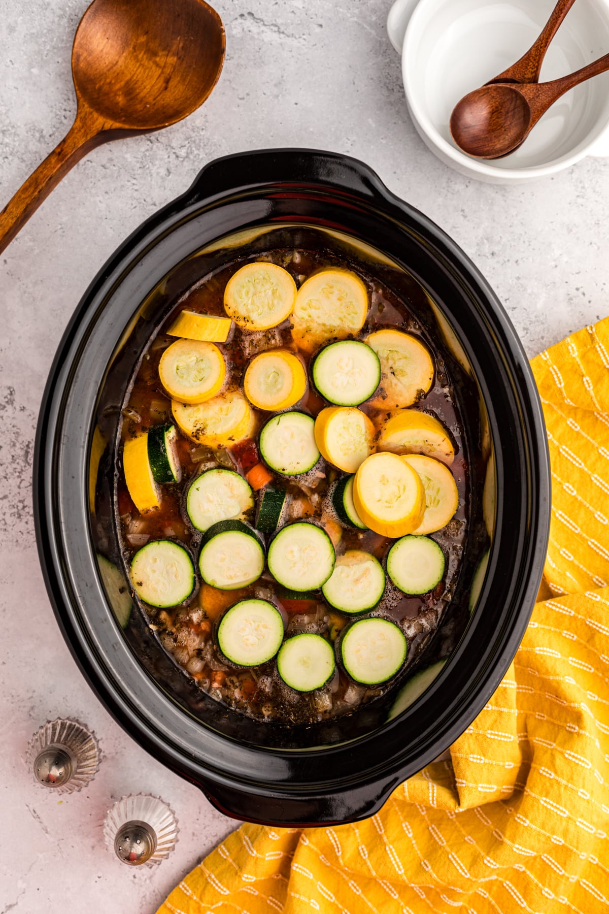 zucchini being added to soup in a slow cooker.