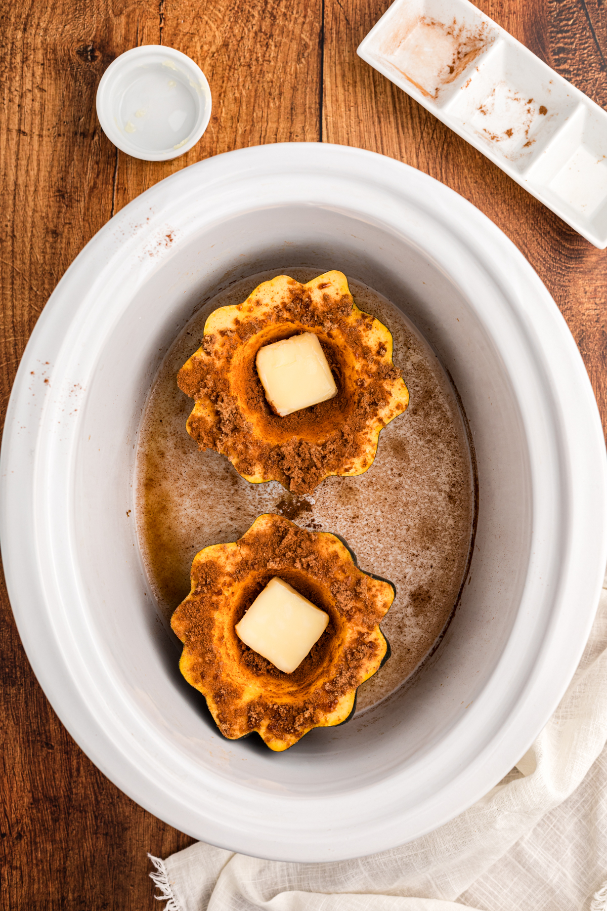 butter added to the center of two acorn squash halves in a slow cooker.