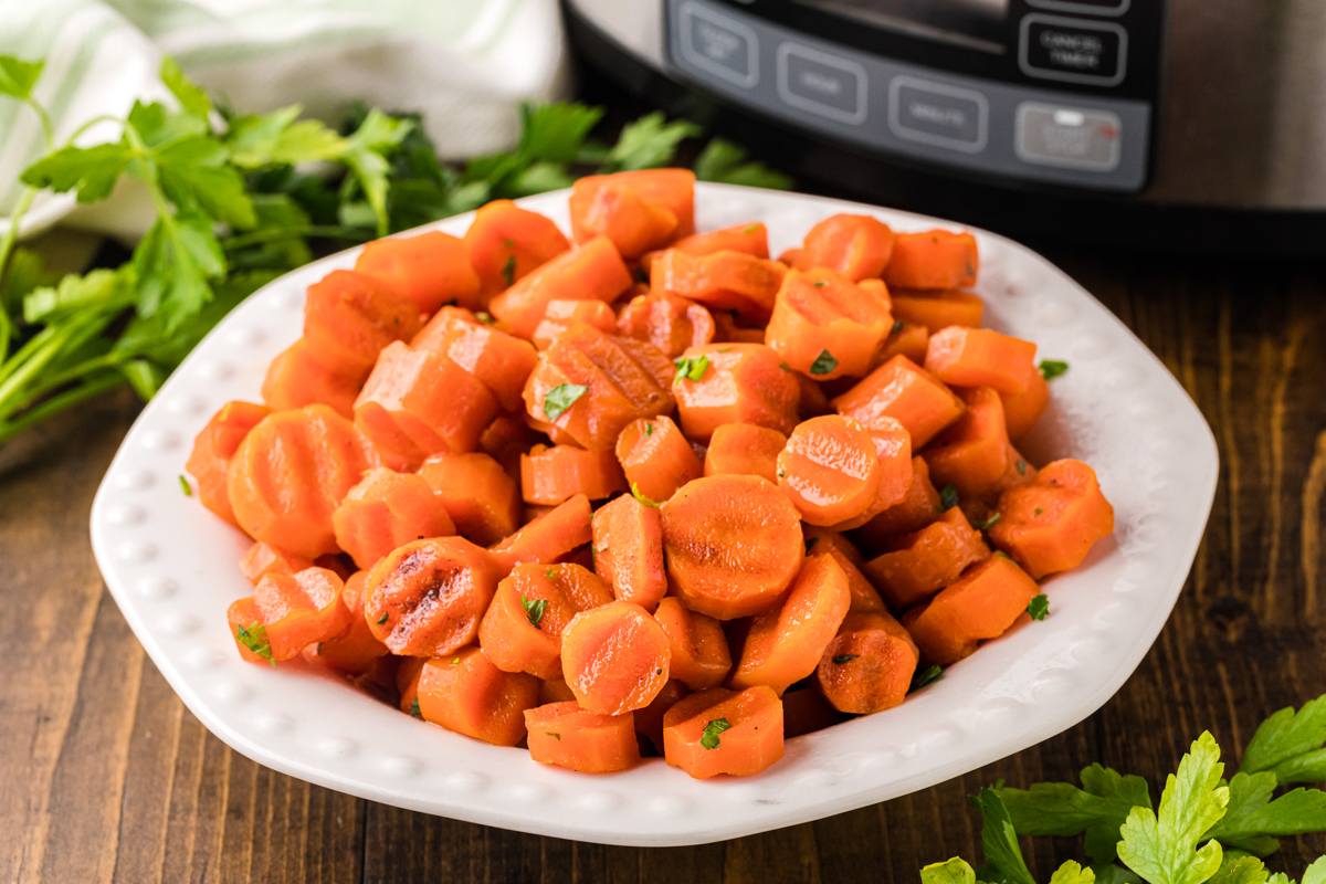 slow cooker candied carrots on a plate in front of a crockpot.