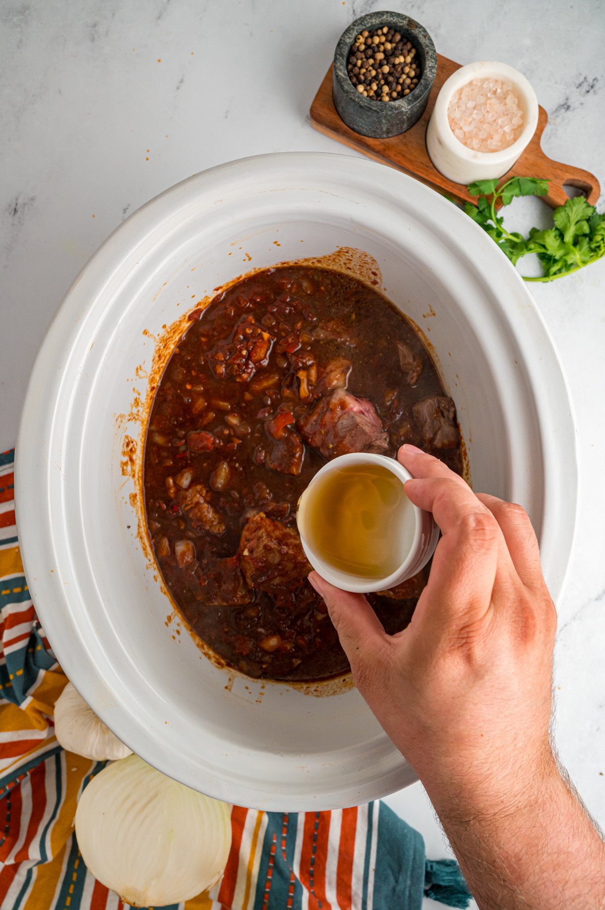 apple cider vinegar being added to the ingredients in a crockpot.