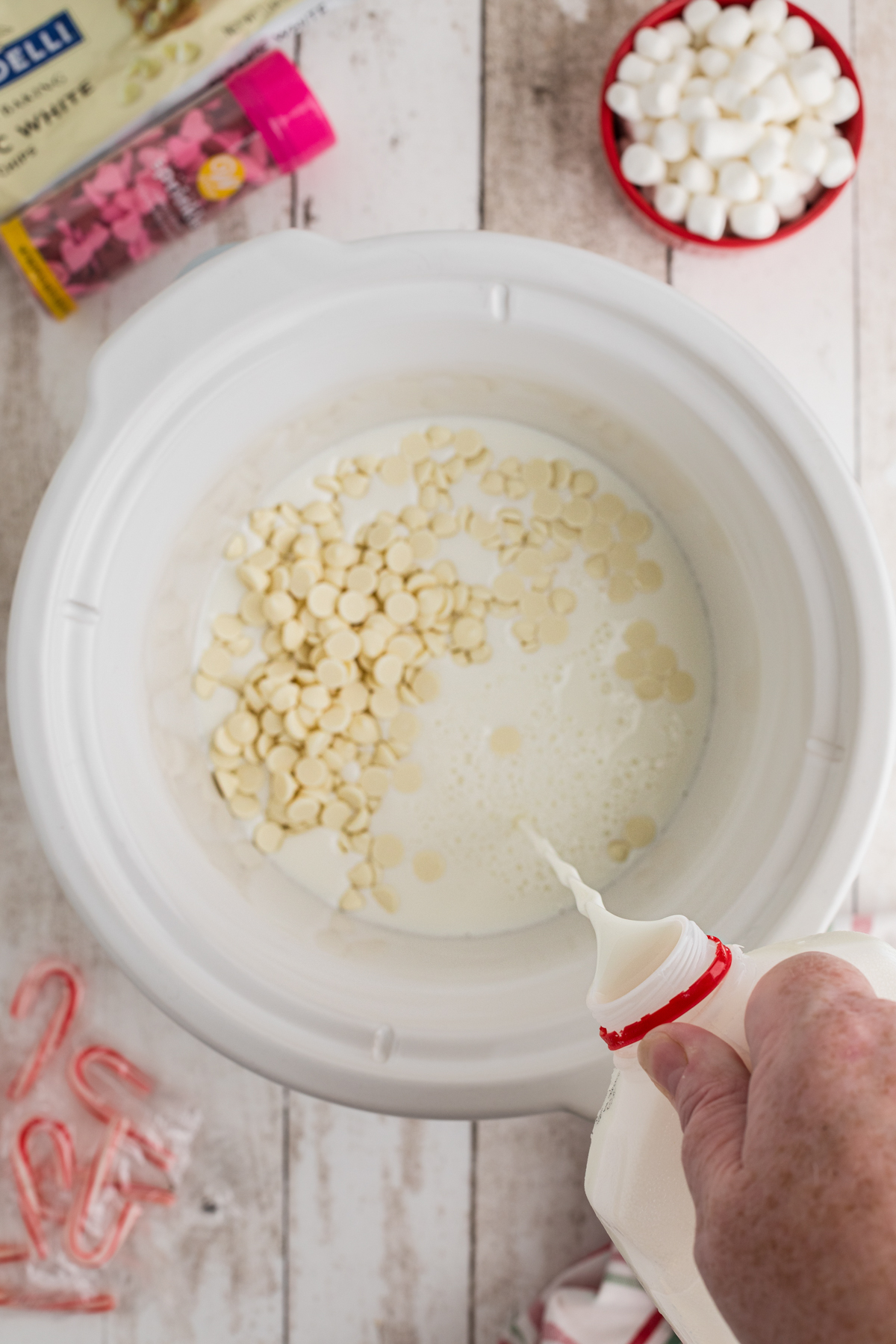 Milk being added to a crockpot with white chocolate chips.