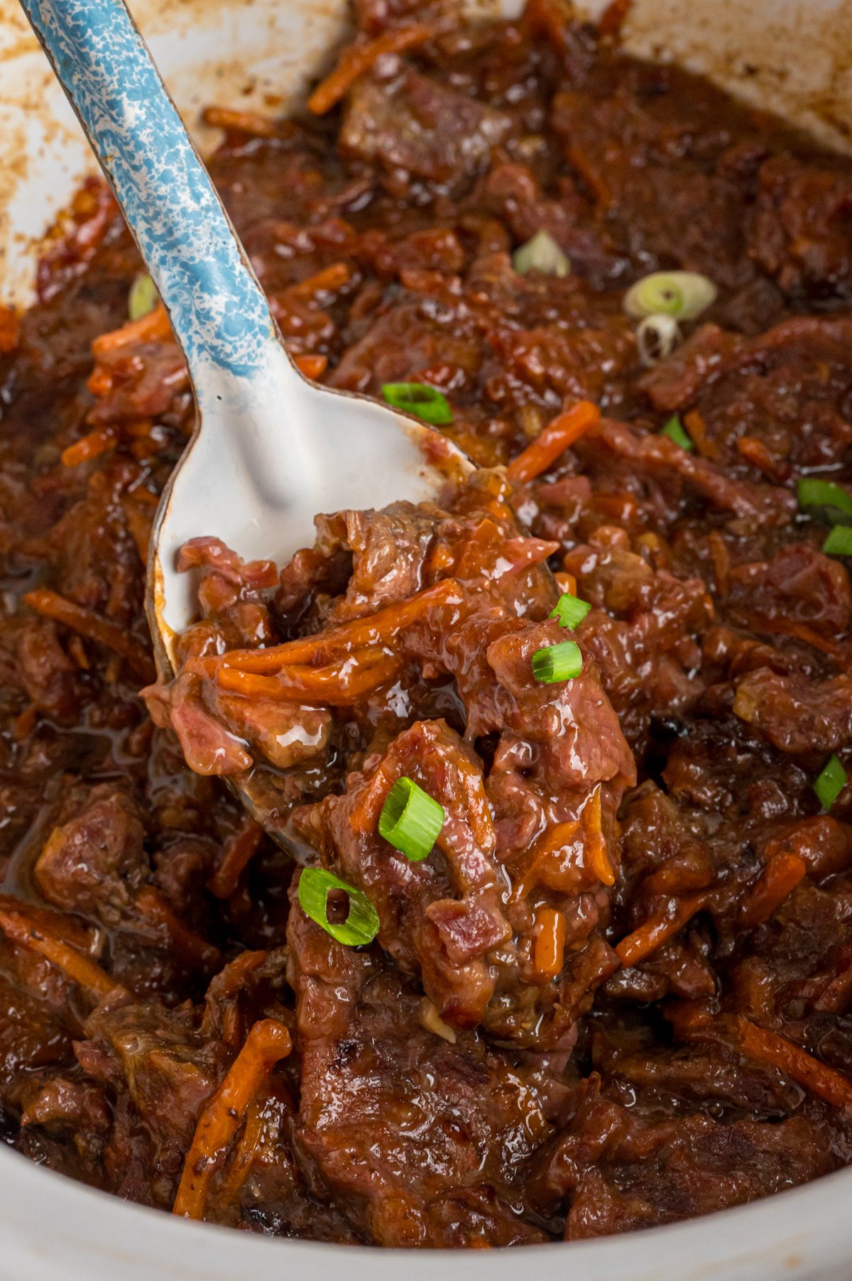 scooping out slow cooker mongolian beef with a large spoon.