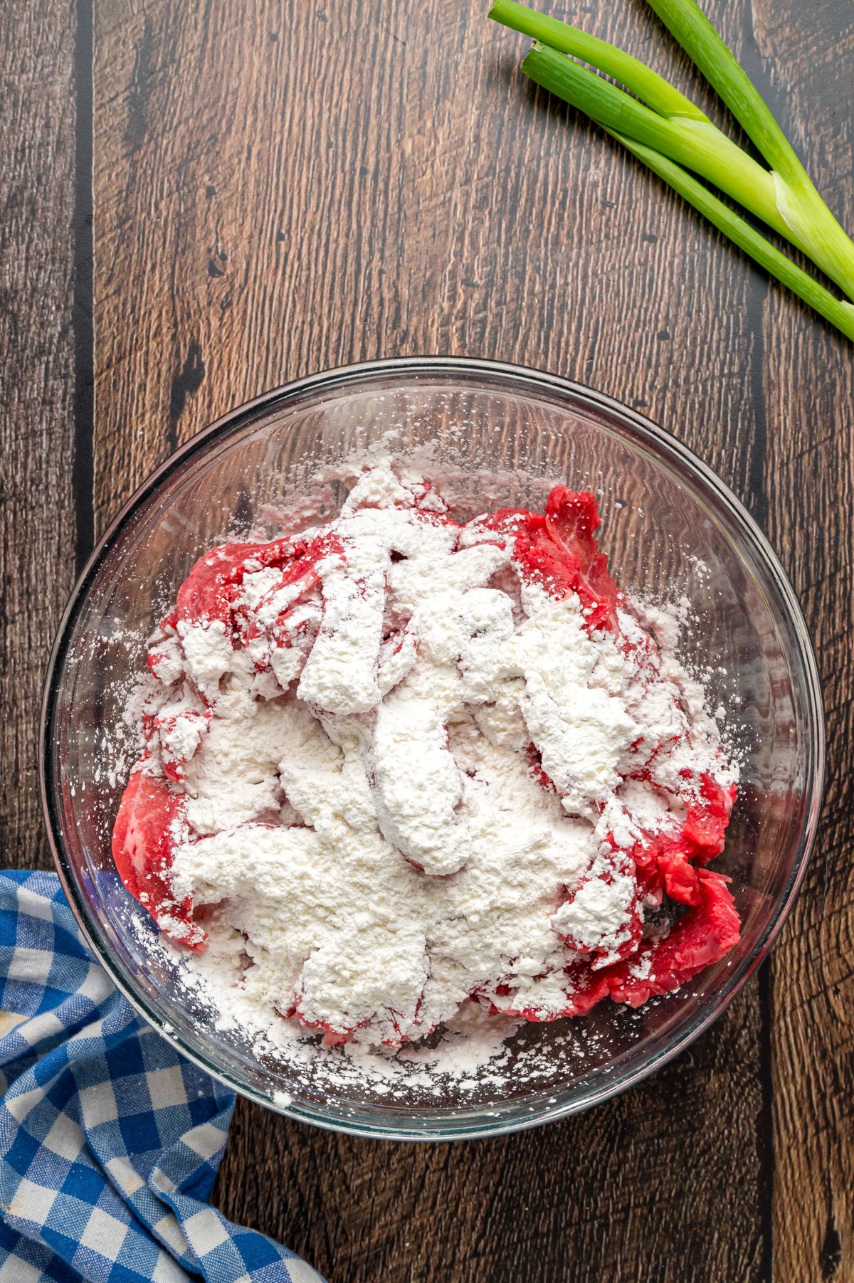 cornstarch and flank steak in a mixing bowl getting ready to combine.