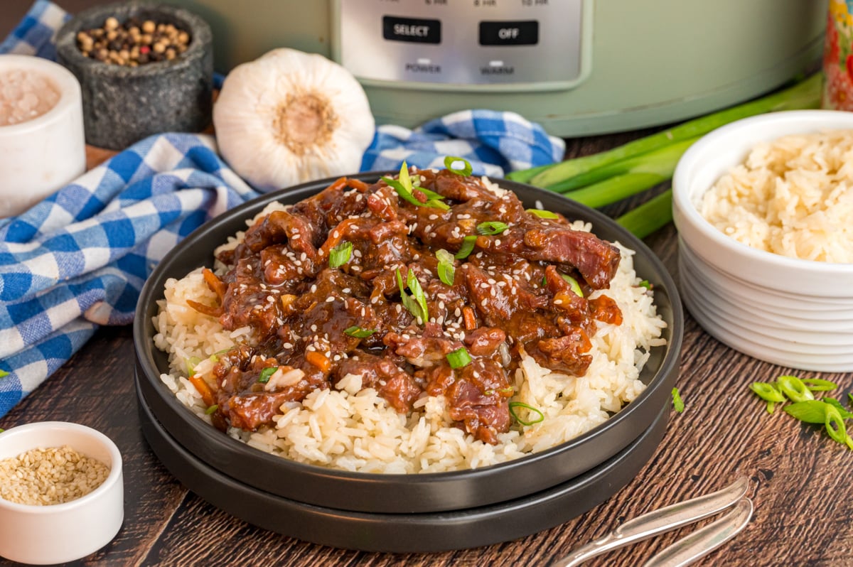 serving of slow cooker mongolian beef over rice in front of a crockpot.
