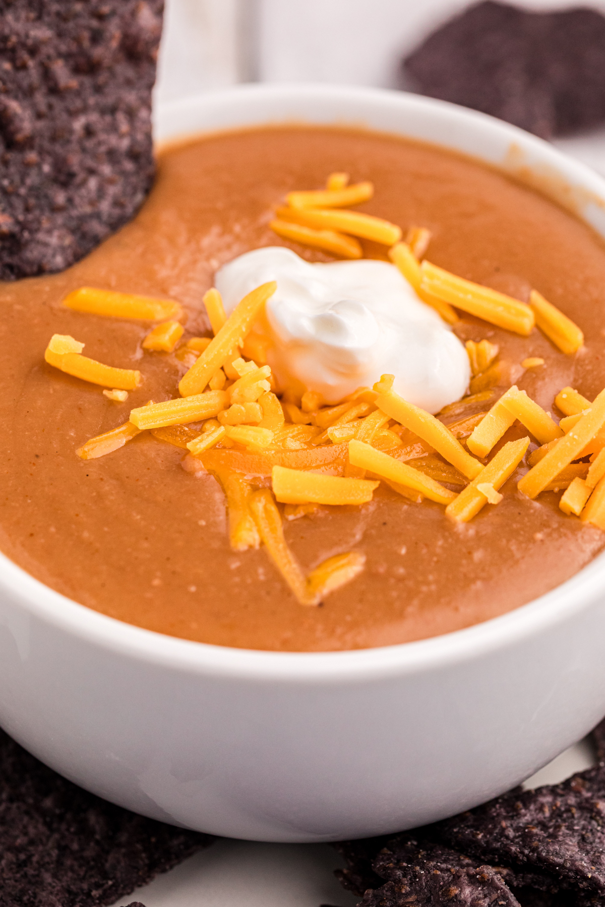close-up of serving slow cooker refried bean soup in a bowl with cheese and sour cream.