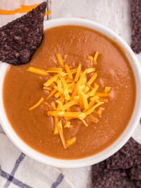 overhead of serving of slow cooker refried bean soup with cheese on top.