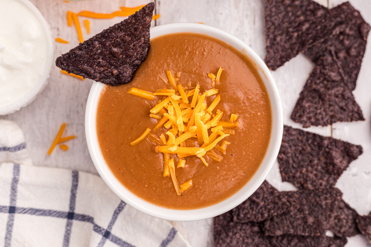 overhead of serving of slow cooker refried bean soup with cheese on top.
