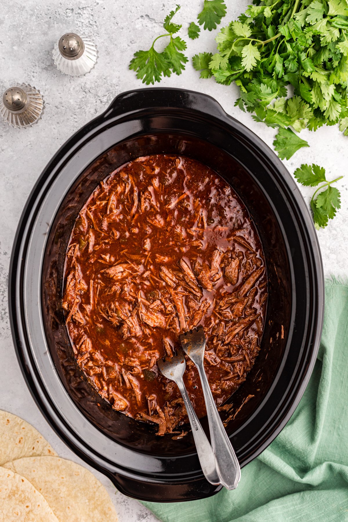 Shredded salsa beef in a crock pot with two forks.