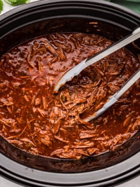 Salsa beef in a slow cooker with tongs in it.