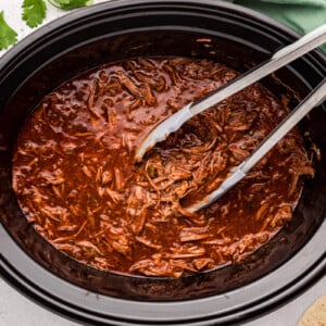 Salsa beef in a slow cooker with tongs in it.