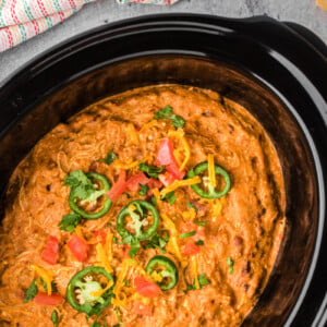 Slow cooker chicken taco dip garnished with jalapenos, tomatoes, and cilantro.