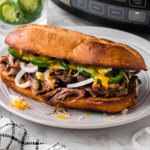 One of the slow cooker jalapeno beef sammies on a white plate in front of a crockpot.