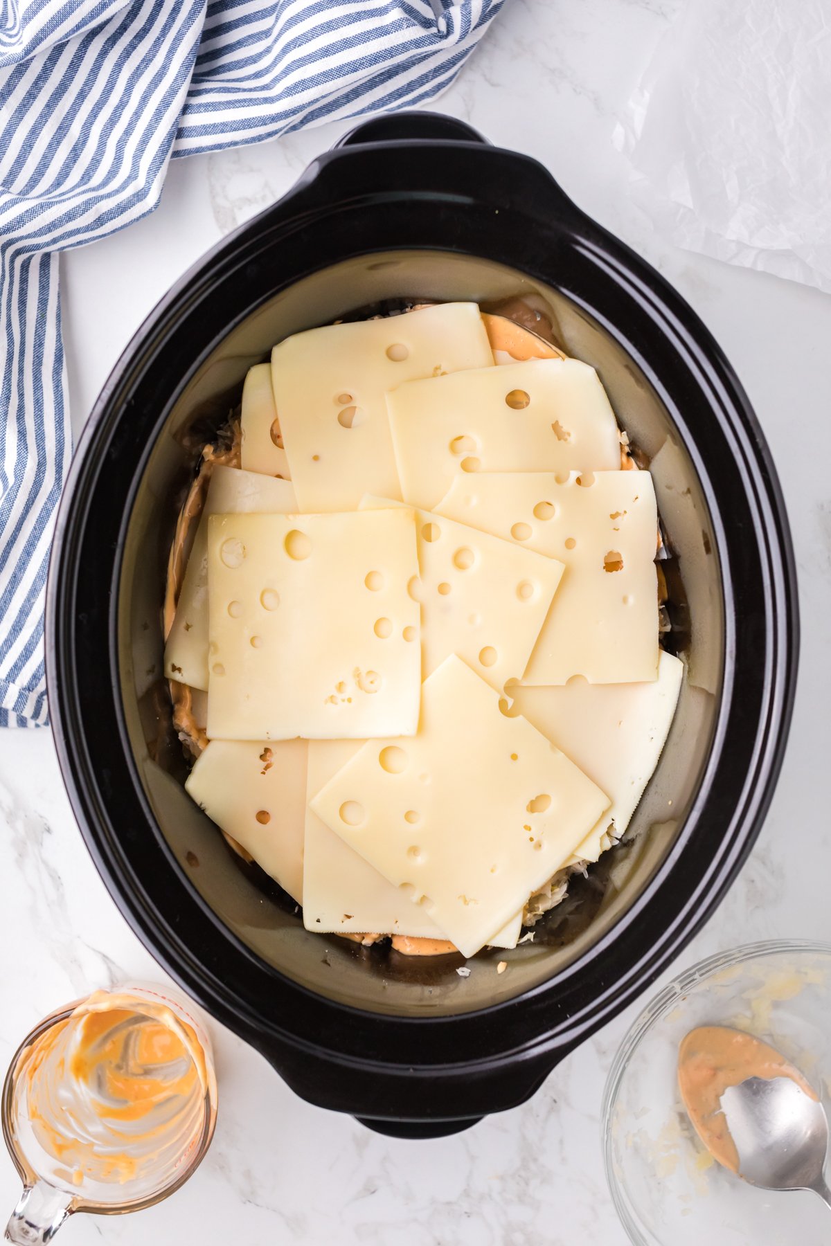 Swiss cheese added on top of chicken, sauerkraut and dressing in a crockpot.