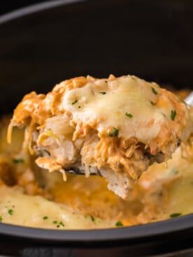 Spoon holding up some slow cooker chicken reuben casserole over a crockpot.