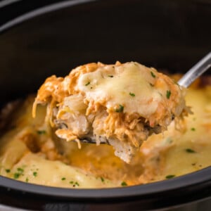 Spoon holding up some slow cooker chicken reuben casserole over a crockpot.
