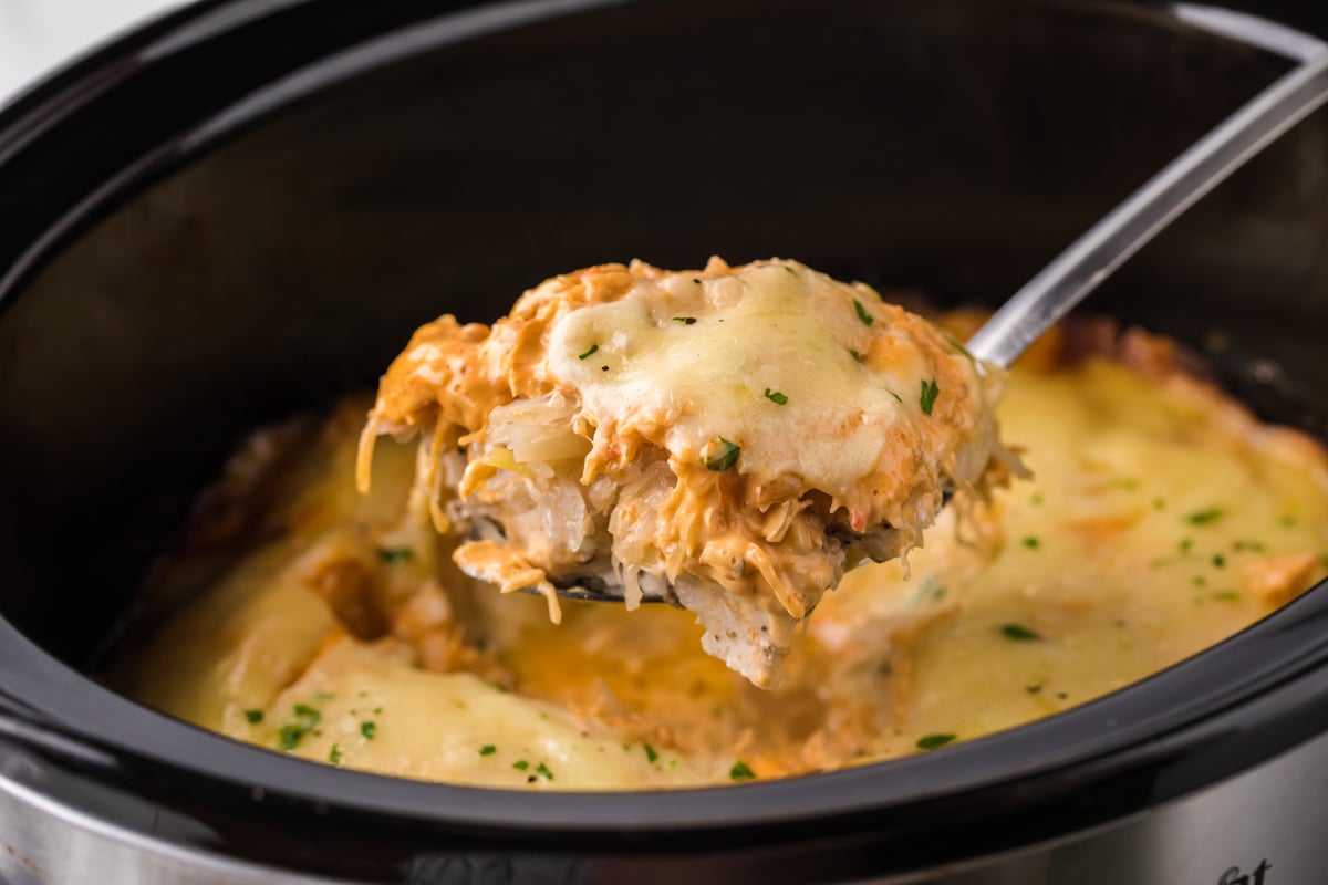 Spoon holding up some slow cooker chicken reuben casserole over a crockpot.